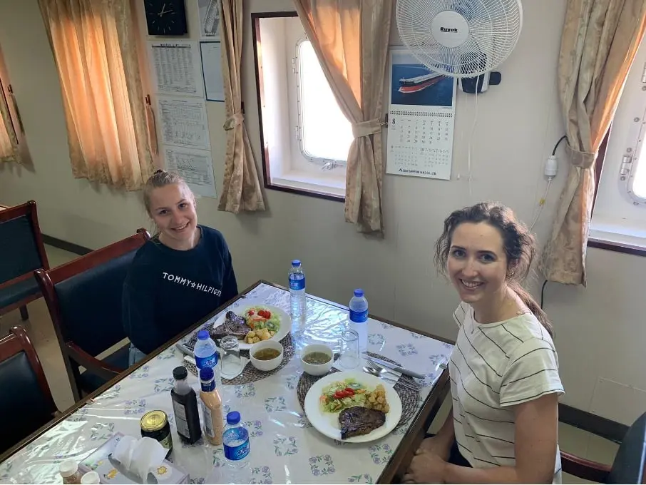 Two women eat at a table in a ship’s galley.