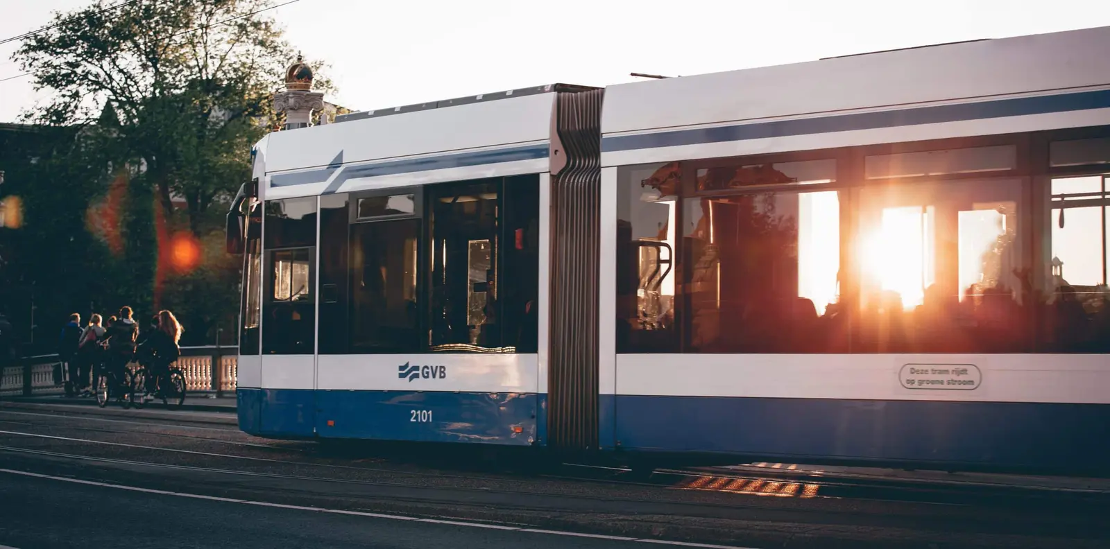 A GVB tram travels through the city with the low sun reflected in its windows.