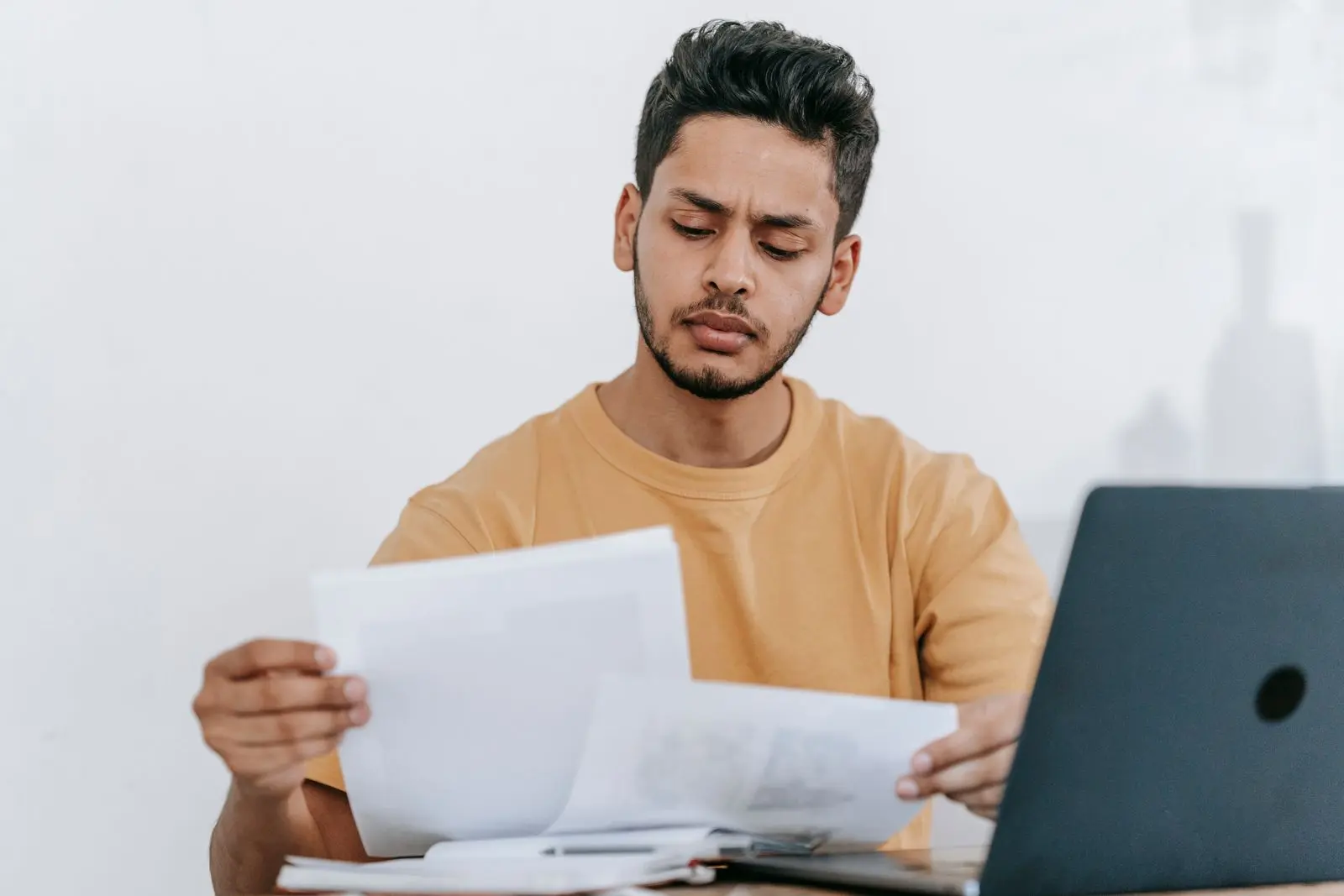 Man vergelijkt met gefronste blik twee uitgeprinte overzichten naast zijn laptop