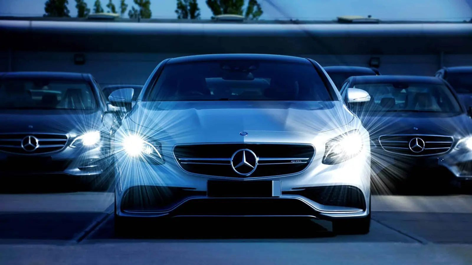 Um Mercedes cinzento-prateado com os faróis acesos no escuro.