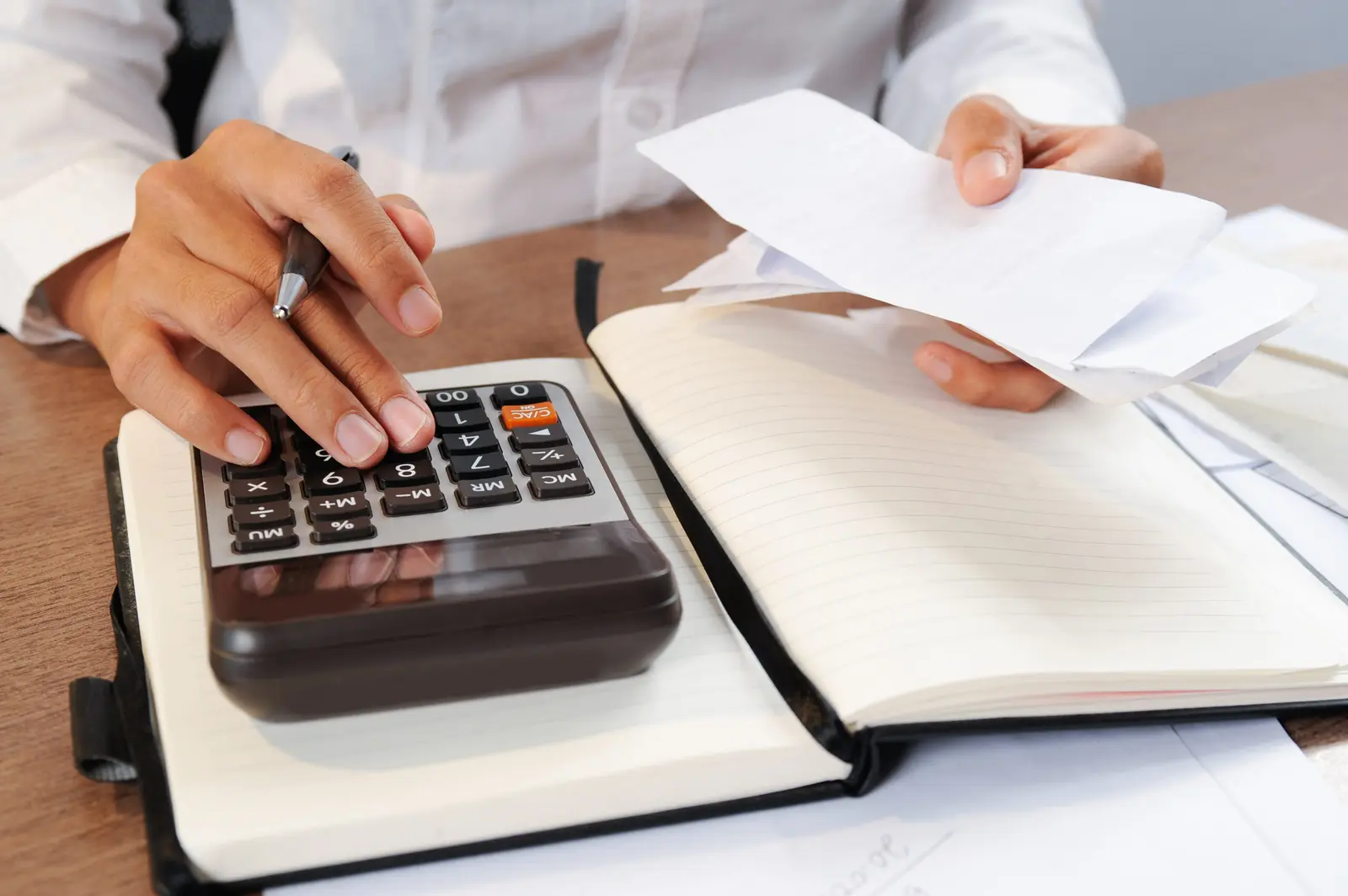 Hands using a calculator beside an open notebook and papers.