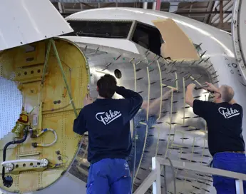 Twee monteurs van Fokker werken aan de binnenkant van een vliegtuigromp.