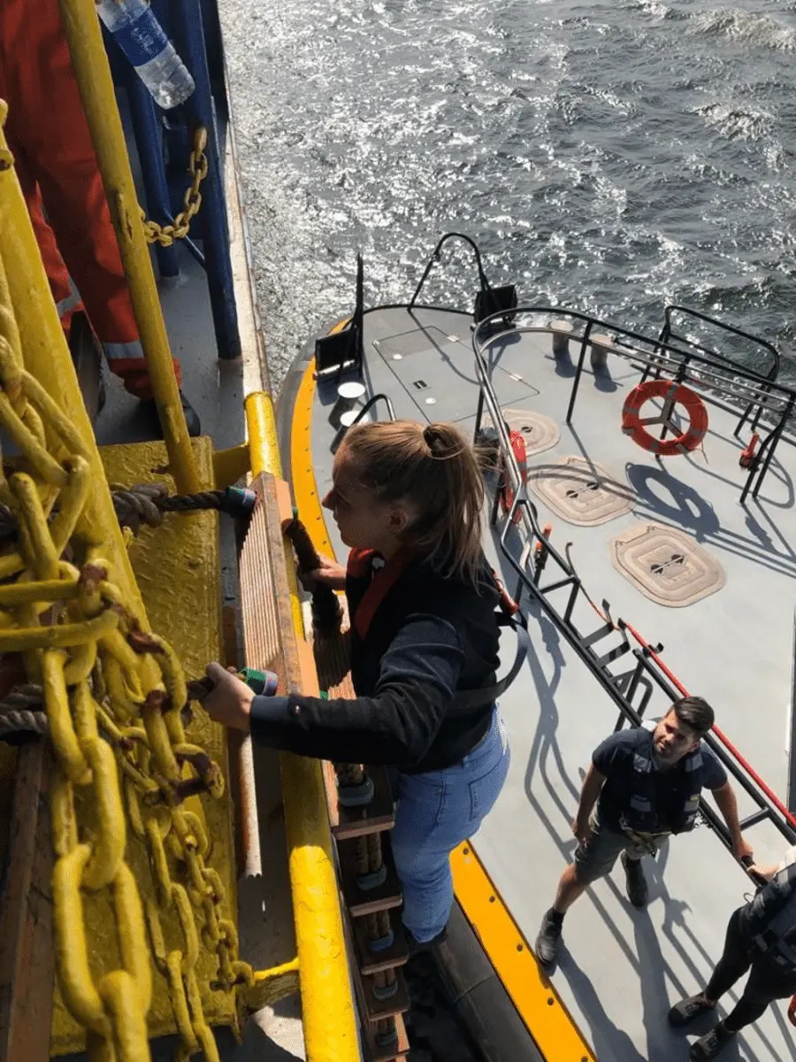 Iemand loopt over het dek van een schip langs een geel gemarkeerde trap.