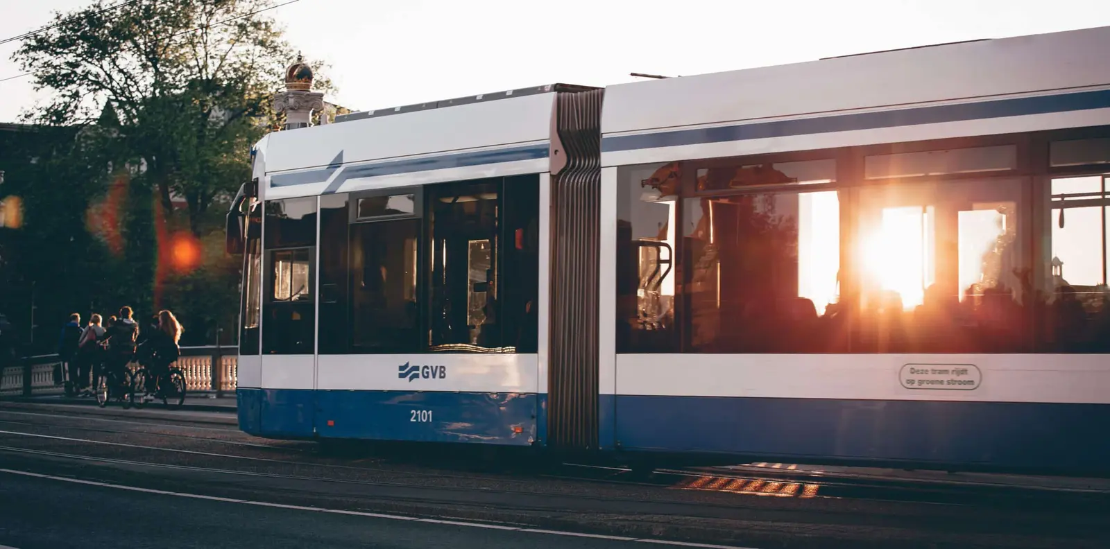 Um elétrico da GVB percorre a cidade com o sol baixo refletido nas janelas.
