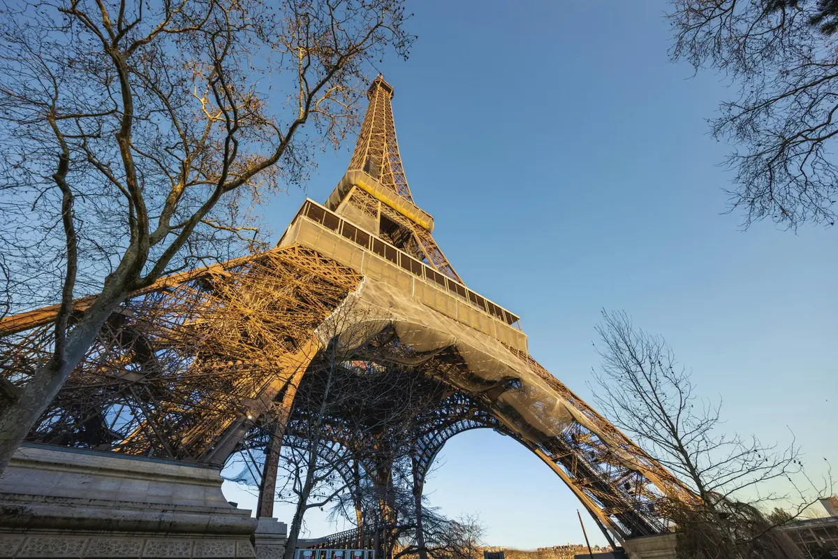 A Torre Eiffel vista de baixo, entre árvores despidas.