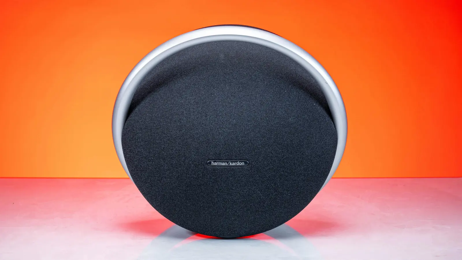 Uma coluna redonda da Harman Kardon sobre um fundo laranja.