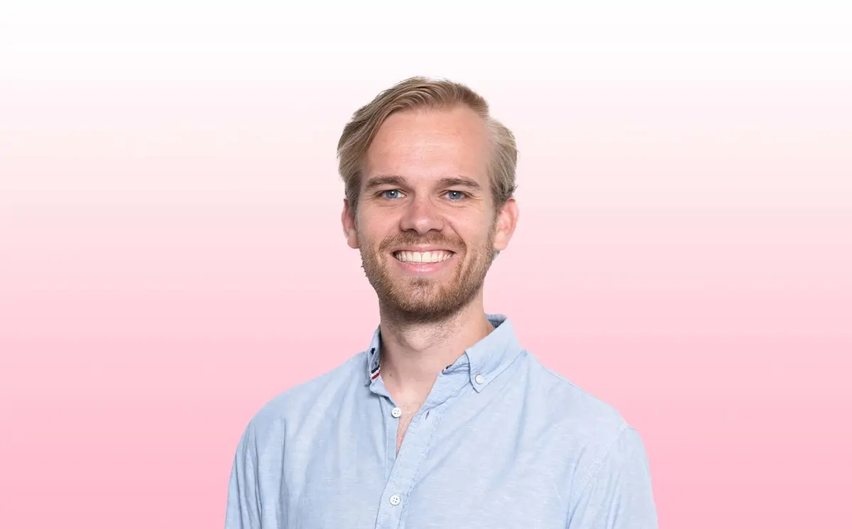 Retrato de um homem sorridente sobre um fundo cor-de-rosa.