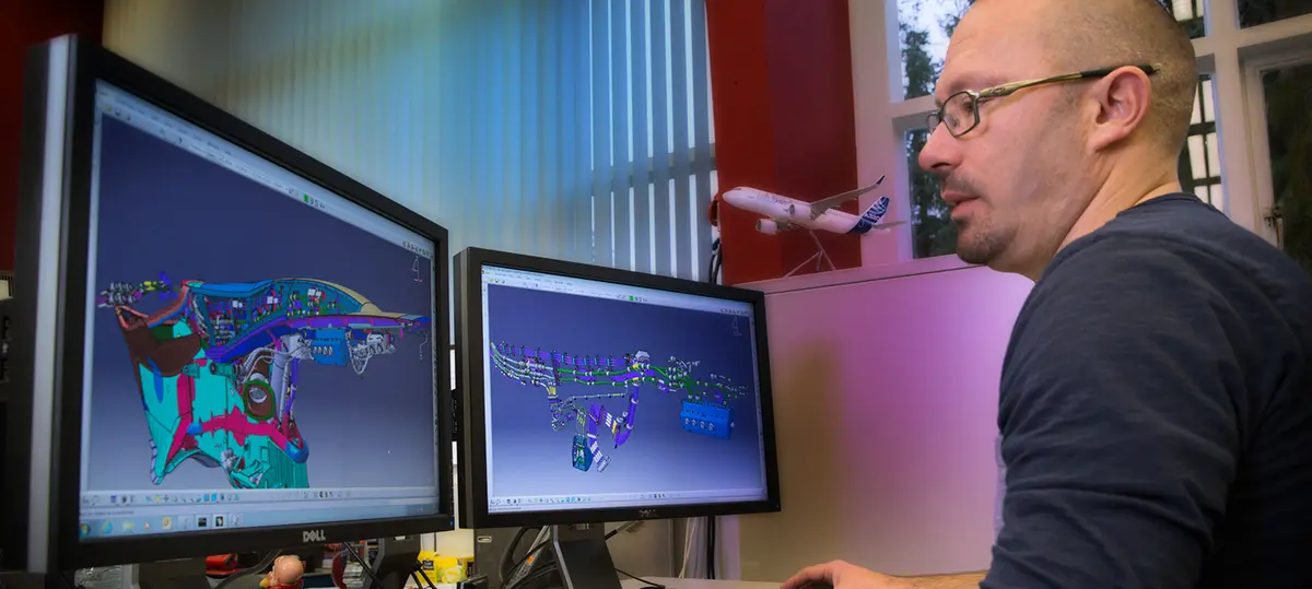Um homem trabalha em dois ecrãs com modelos tridimensionais de aviões.