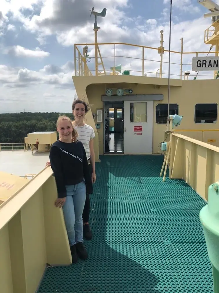 Two women stand on the deck of a ship near the superstructure.