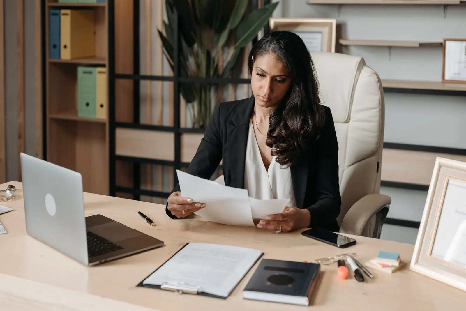 Medewerker aan haar bureau leest een document na, met een laptop en paperassen ernaast
